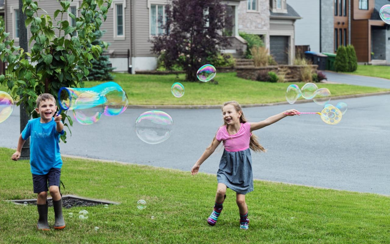 Deux enfants font des bulles devant une maison