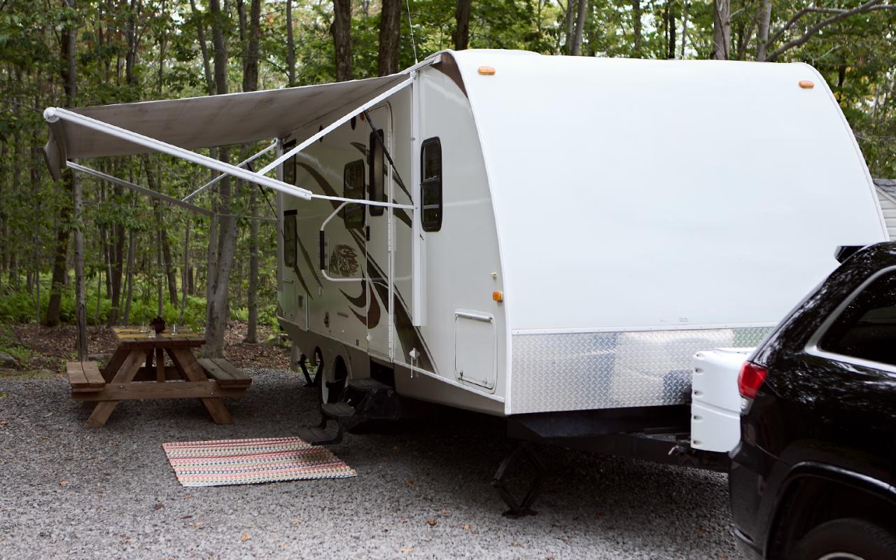 Une caravane devant le bois avec un auvent déployé